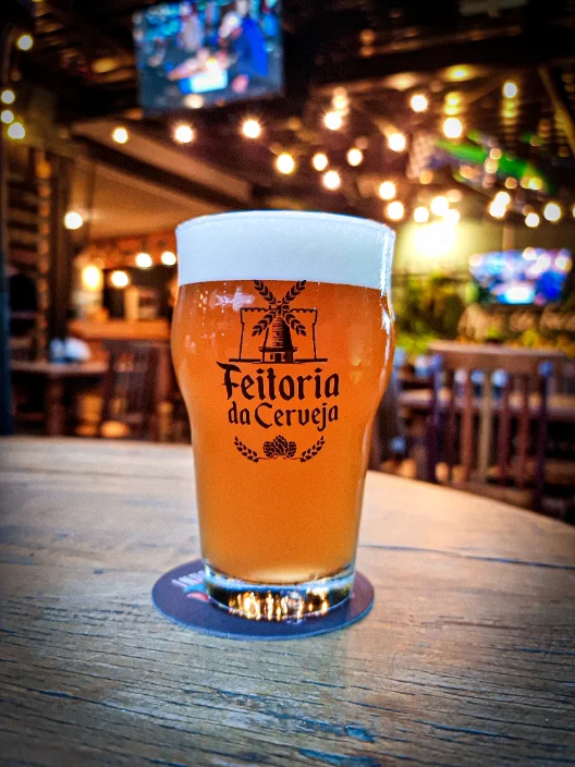 Copo de chopp claro da Feitoria servido na mesa do quintal