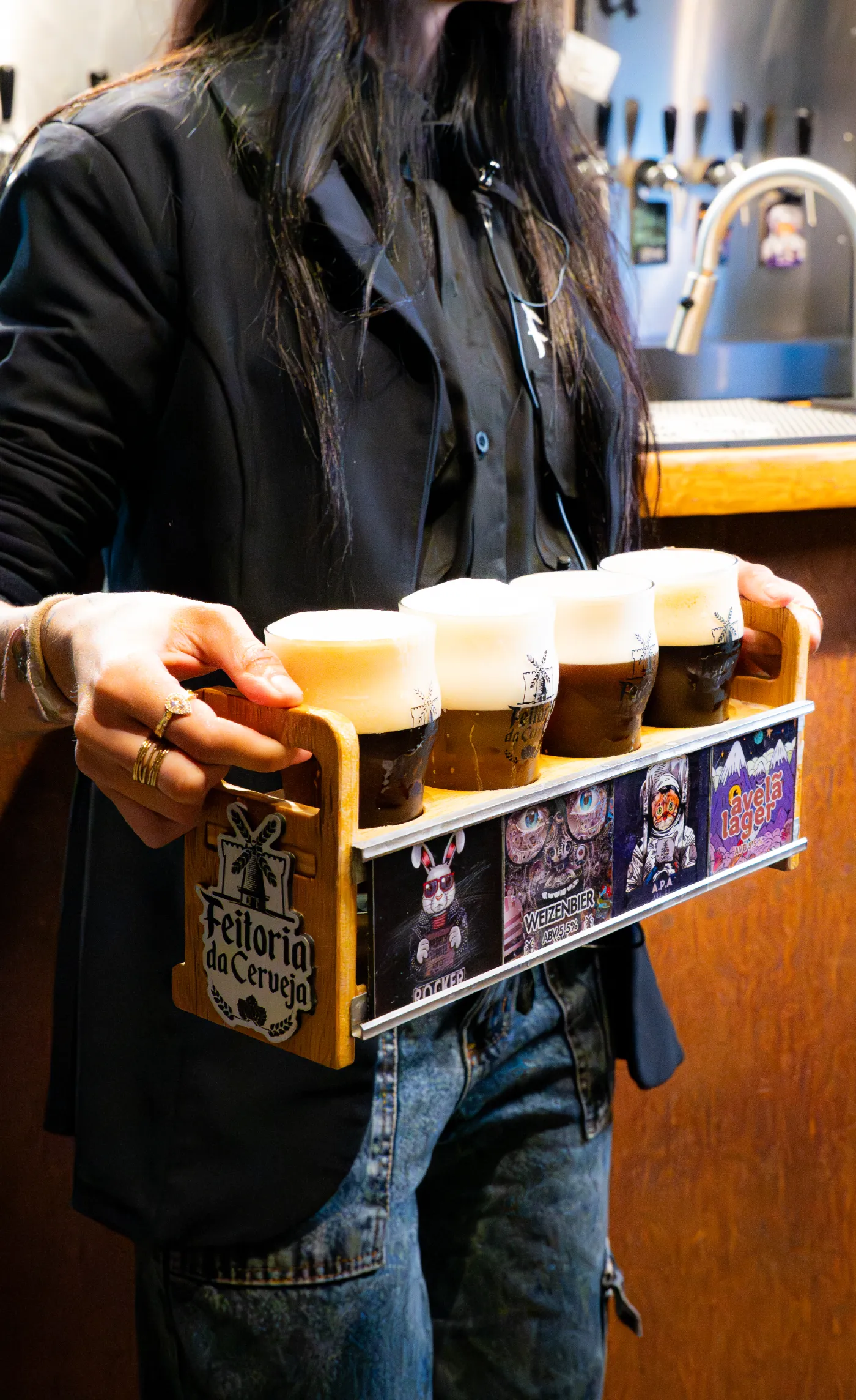 Régua de degustação com quatro copos de chopp segurada na mão
